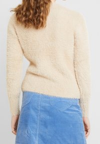 Krämsfärgad, fluffig stickad tröja med långa ärmar och rund halsringning, parat med en ljusblå corduroy kjol med bakfickor.