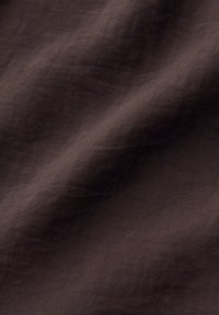 Dark brown fabric with visible texture and soft wrinkles creating subtle folds across the surface.