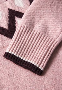 Stickad rosa tröja med ribbade maroon-muddar med vita detaljer och ett kontrasterande geometriskt mönster i mörklila och kräm.