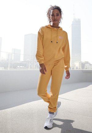 Yellow hoodie with a front pocket and drawstrings, paired with matching jogger pants. Both pieces have a textured fabric and relaxed fit.