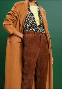 Kameelwollen jas, zwart-wit gestreepte shirt, gele top en bruine suede broek; heeft een lange, op maat gemaakte ontwerp en zichtbare zakken.