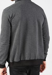 Chaqueta de punto gris con una superficie texturada, con un alto cuello y puños y cintura de canalé negros. La vista posterior muestra un diseño ajustado.