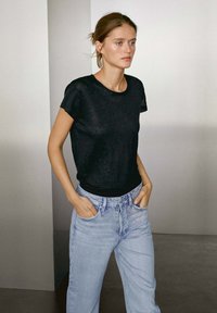 Zwarte t-shirt met korte mouwen van een iets transparante stof, gecombineerd met hoogbegaafde, lichtblauwe denim jeans.
