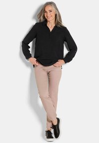 Schwarzes langärmliges Polohemd mit Kragen, kombiniert mit hellbeigen, figurbetonten Hosen und schwarzen Sneakers. Einfaches Design mit klaren Linien und minimalen Details.