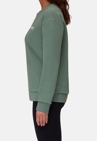 Zielona bluza z okrągłym dekoltem, długimi rękawami, ryflowanymi mankietami i dołem. Posiada małe logo z przodu. Miękka, fakturowana tkanina.