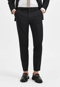 Svarte skreddersydde bukser med en jevn tekstur, slim fit, sidelommer, med en pressenning nedover bena, sammen med glansfulle svarte loafers.