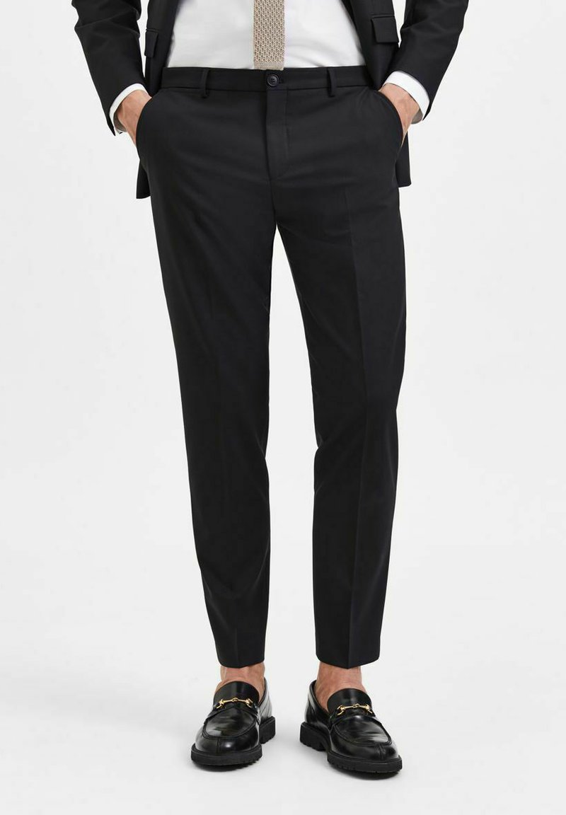 Svarte skreddersydde bukser med en jevn tekstur, slim fit, sidelommer, med en pressenning nedover bena, sammen med glansfulle svarte loafers.