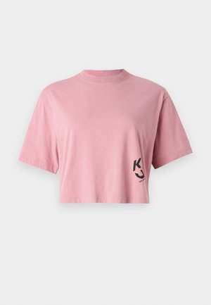 T-shirt court en coton rose doux avec des manches courtes et un col rond. Présente un logo noir sur le bas à gauche.