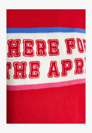 Rdeč pulover z drznim, rdečim vezenim napisom "TUKAJ ZA APR" na belem ozadju, okrašen z modrimi in roza črtami.