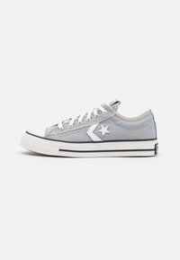 Baskets basses en toile grise avec des lacets blancs, un logo d'étoile blanche sur le côté et une semelle en caoutchouc blanche avec des rayures noires.