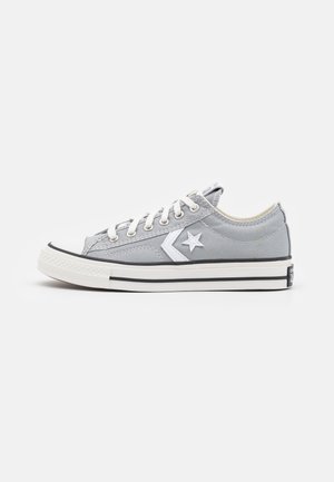 Sneaker grigia in tela a low-top con lacci bianchi, un logo a stella bianca sul lato e una suola in gomma bianca con strisce nere.