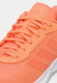 Κοντινό πλάνο ενός φωτεινού πορτοκαλί παπουτσιού για τρέξιμο με κορδόνια, επενδεδυμένη γλώσσα και λευκή σόλα.