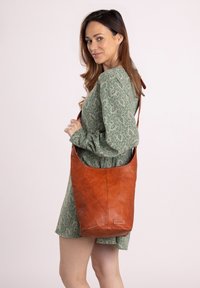 Brown leather shoulder bag with a slouchy design, featuring a single strap and a textured surface. Accented with a brand label.