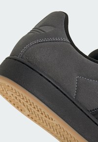 Γκρι σουέτ παπούτσι με υφή μαύρης καουτσούκ σόλας και αντίθετη λευκή ραφή, με μινιμαλιστικό σχεδιασμό και στρογγυλεμένη μύτη.