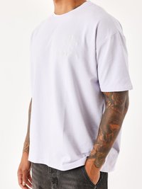 Camiseta de algodón de color púrpura claro con un sutil diseño bordado de un globo y texto en el lado izquierdo del pecho. Mangas cortas y corte relajado.