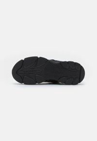 Black rubber sneaker sole with textured patterns and grooves; features brand name "LACOSTE" embossed on the surface.