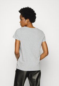 Grå bomulds T-shirt med korte ærmer, rund halsudskæring og en diskret logo detalje nær kanten. Sammen med sorte læderbukser.