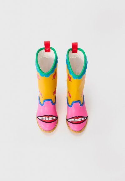Colorful rubber rain boots, yellow with pink and blue accents, featuring smiling mouth designs and star patterns. Red pull tabs at the top.
