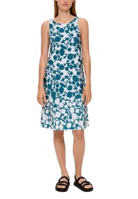 Ärmelloses Kleid mit einem tealfarbenen Blumenmuster auf hellem Hintergrund. A-Linie, knielang, kombiniert mit schwarzen Riemchensandalen.