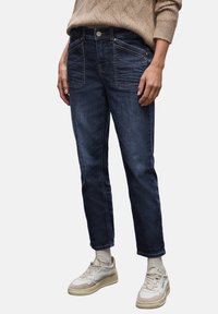 Pantalones vaqueros de denim azul oscuro con corte recto, que cuentan con bolsillos frontales, detalles de costura y un desvanecimiento sutil. Combinados con zapatillas ligeras.