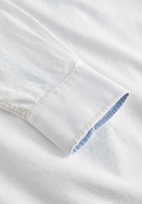 Weißer Hemd cuff mit einer hellblauen karierten Innenauskleidung. Glatte Baumwolltextur mit kontrastierender Naht am Rand.