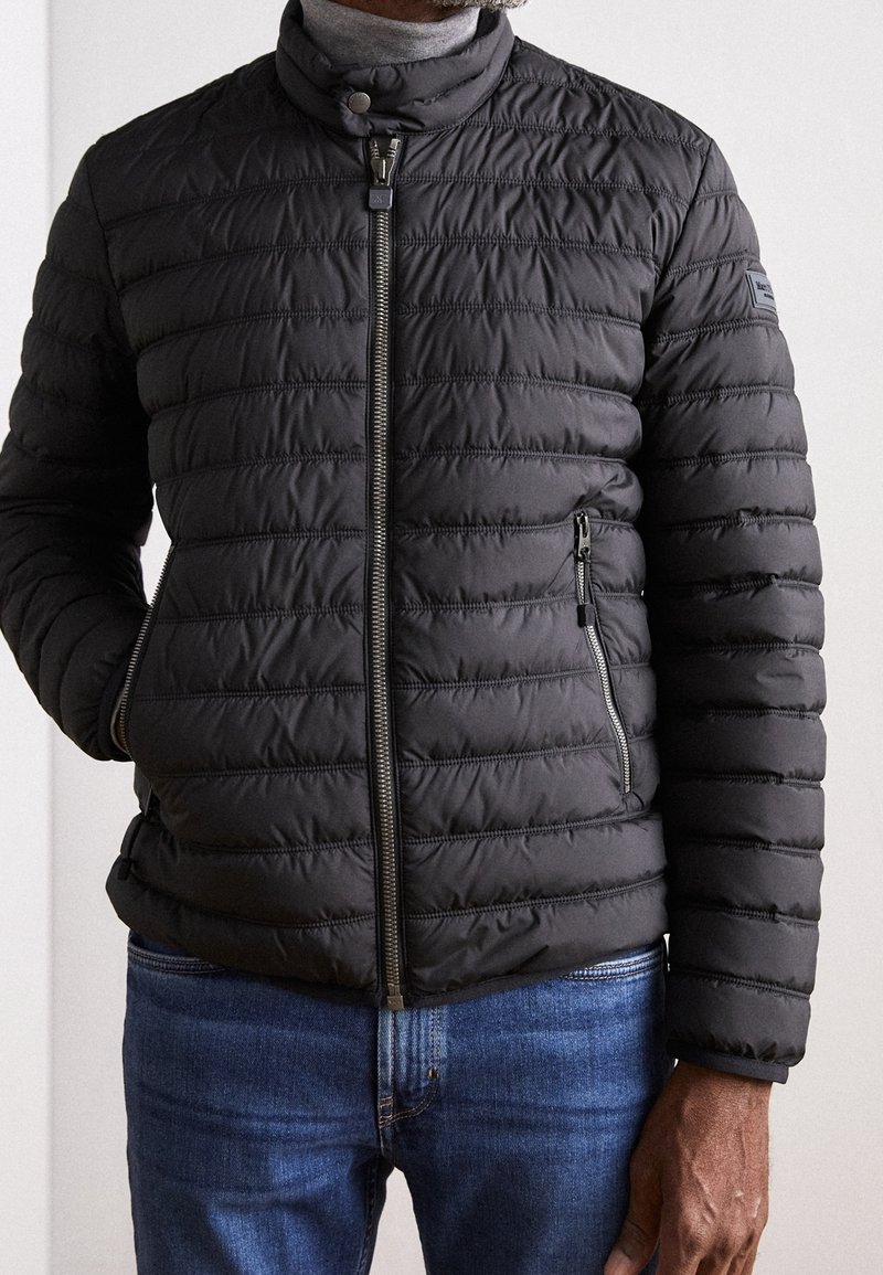 Veste matelassée noire avec un col montant, une fermeture éclair devant et des poches latérales zippées ; présente une surface lisse et texturée.