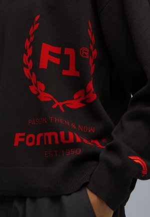Zwarte gebreide trui met rode geborduurde logo's: "F1®," laurierontwerp en "Formular" met "EST. 1950," textuurstof, relaxte pasvorm.