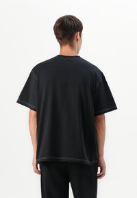 Svart oversized bomull T-skjorte med korte ermer, kontrasterende hvit søm og en enkel, rund halslinning. Har en avslappet passform.