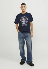 T-shirt en coton navy avec impression graphique présentant un design coloré, associé à un jean droit bleu clair et des chaussures noires.