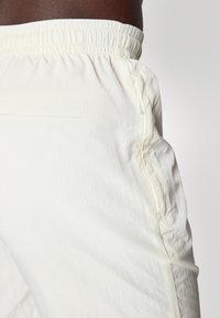 Lyscremefarvede bukser med en samlet elastisk talje, sidelommer med lynlås og et blødt, struktureret stof.