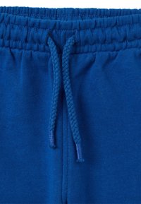 Joggers en coton bleu avec une taille côtelée et un cordon de serrage tressé. Le tissu a une texture lisse avec une couleur uniforme.