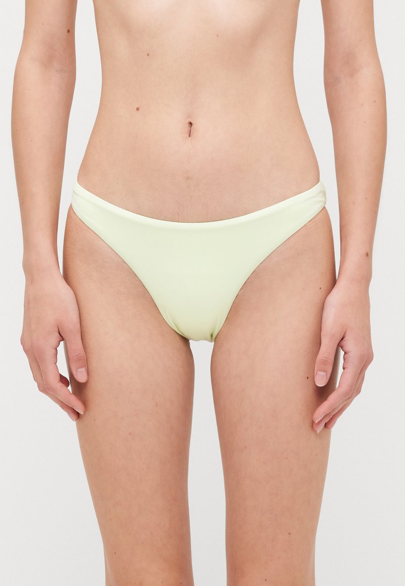 Dzelteni bikini apakšda ar gludu tekstūru, zemu jostasvietu un minimālu pārklājumu. Iezīmējas ar izliektiem sānu šuvēm, nodrošinot bezšuvju izskatu.