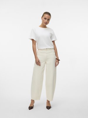 White short-sleeve t-shirt paired with cream wide-leg pants, featuring a high waist. Model stands in brown heeled mules, with a neutral background.