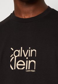 Svart bomulls-t-shirt med en beige Calvin Klein-logotypdesign. Rundad halsringning med en mjuk textur, som visar modern typografi.