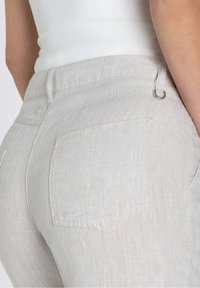 Primo piano di pantaloni beige chiari con cuciture della tasca posteriore e dettagli in metallo, indossati con una maglietta bianca.