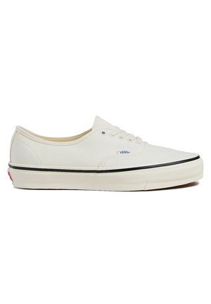 Canvas sneakers in cream color with black trim, lace-up design, and rubber sole. Logo detail on side and textured upper material.