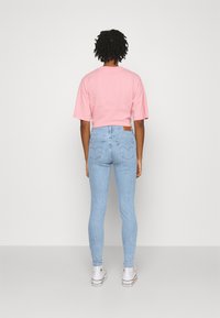 Ljusblå smala jeans med en beige läderlapp, tillsammans med en kortärmad rosa t-shirt. Vita sneakers är på fötterna.