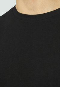 T-shirt noir à col rond fabriqué en coton doux et texturé. Il présente une coupe classique sans motifs ni embellissements visibles.