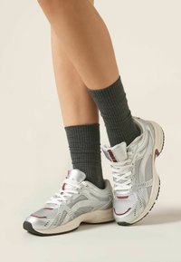 Zapatillas deportivas plateadas con paneles de malla, cordones blancos y suelas de goma gris, combinadas con calcetines de punto de color gris oscuro.