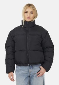Giubbotto imbottito nero con collo alto, zip frontale e maniche ampie. Presenta una vestibilità cropped e un materiale morbido e lucido.