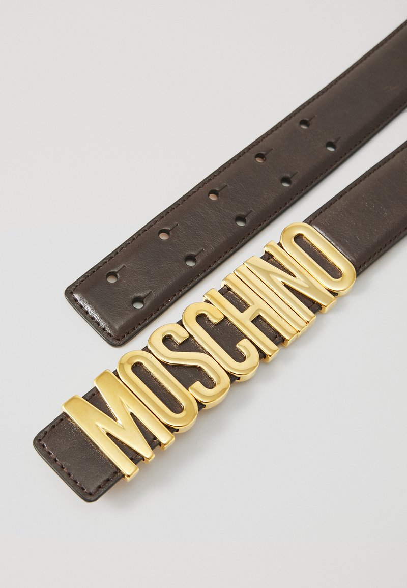 Brown leather belt featuring a bold gold "MOSCHINO" logo buckle, with evenly spaced holes for adjustment. Smooth texture with polished finish.