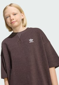 Preveliki tamno smeđi pamučni majica s okruglim izrezom, sa bijelim Adidas logotipom na prsima i kratkim rukavima.