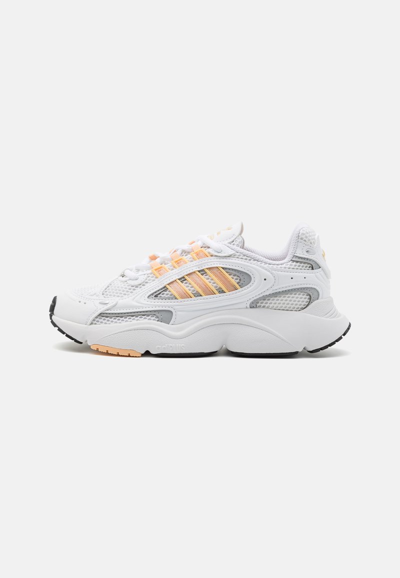 White athletic shoe with mesh and synthetic materials, featuring orange accents, three-striped design, rounded toe, and textured sole.