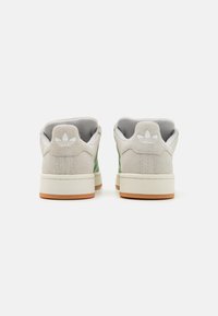 Baskets avec une tige en suede gris clair et des accents verts, semelle en caoutchouc blanc et semelle extérieure en gomme beige, affichant un logo sur le talon.