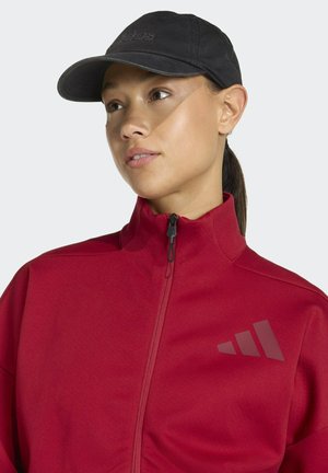 Chaqueta deportiva roja con cremallera, hecha de un material suave, que cuenta con una gorra negra y un logo en gris oscuro en la parte izquierda del pecho.