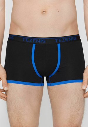 Torace maschile con boxer neri con rifiniture blu e logo blu "TEZENIS" in vita, mani appoggiate accanto alle cosce.