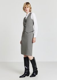 Ensemble jupe et gilet à rayures grises, à la coupe ajustée, associé à des bottes en cuir noir à hauteur de genou avec un accent subtil.
