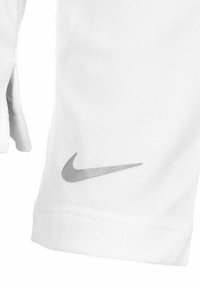 Manchon de sport blanc, fabriqué en tissu texturé, arborant un logo Nike gris sur le poignet. Design structuré avec un détail de fente ouverte.