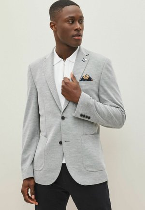 Gray textured blazer with two front pockets, single-button closure, and a patterned pocket square. Paired with a white collared shirt.