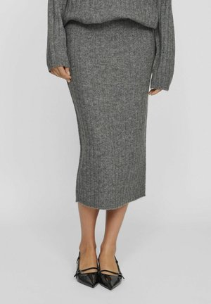 Falda de punto gris con canalé de largo a media pantorrilla, con un dobladillo ligeramente desflecado. Combinada con unos zapatos negros brillantes de punta afilada.